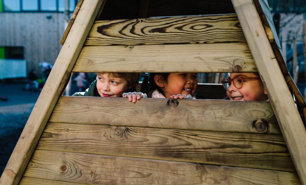 Lachende kindjes kijken door een spleet in een houten constructie