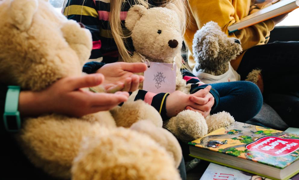 Drie kinderen op een rij met beren en boeken over geloof