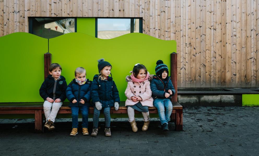 Kinderen zitten op een rijtje op een bank op de speelplaats