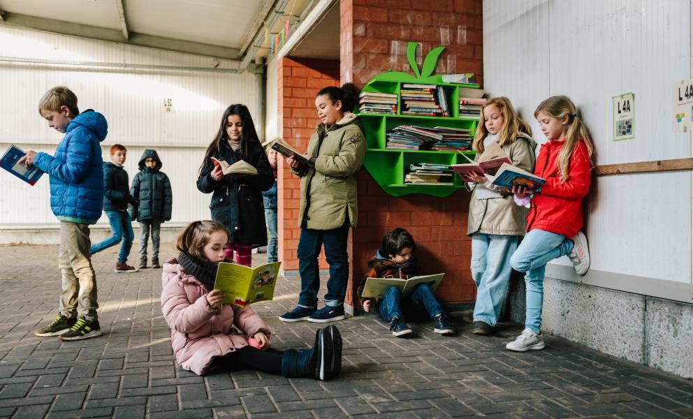 Groepje oudere leerlingen leest boeken op de speelplaats