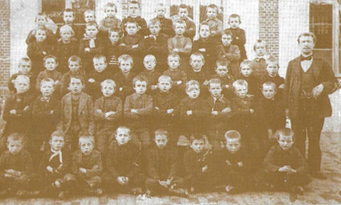 Klasfoto van meester Knapen met een zomerse klas van 47 leerlingen op de ‘koer’ van de toenmalige gemeentelijke jongensschool in de Schoolstraat, nu Kasteeldreef