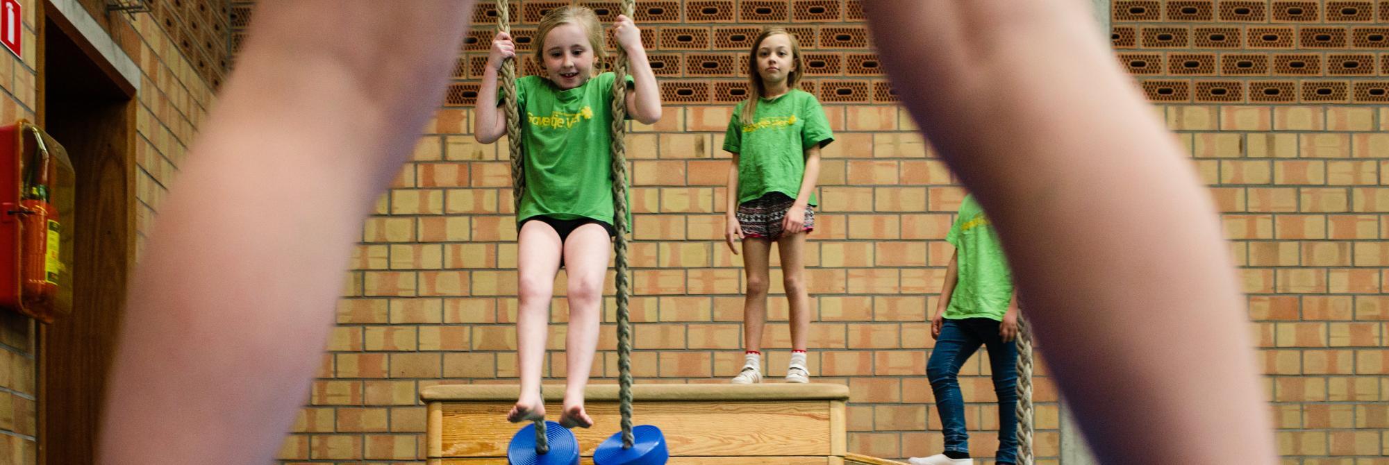 Kinderen zwieren aan touwen, gezien door benen van ander kind